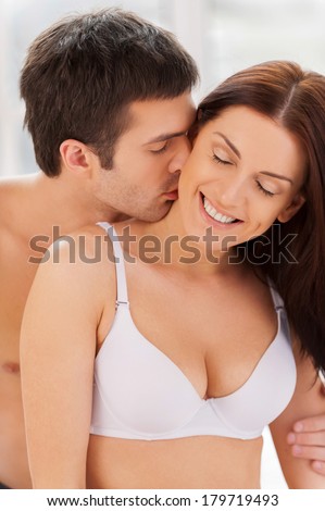 I love him doing it! Beautiful young loving couple sitting together in bed while man kissing his girlfriend at neck