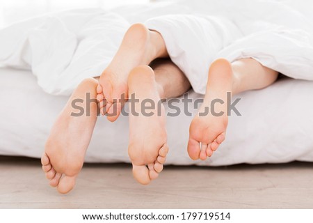 Feet from the blanket. Close-up of female and male feet stretching out from the blanket