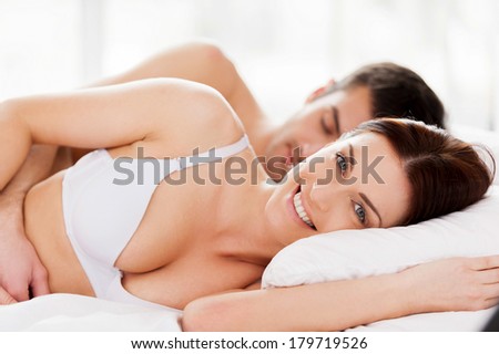 Loving couple in bed. Beautiful young loving couple lying in bed while woman looking at camera and smiling