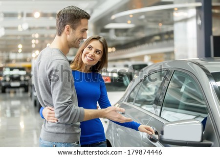I like this car. Beautiful young couple standing at the dealership choosing the car to buy