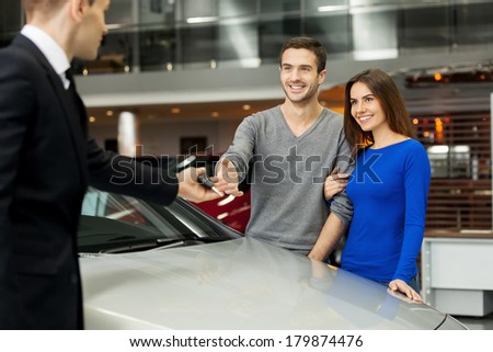 They have made a right vehicle choice. Young car salesman giving a key from the new car to the beautiful young owners