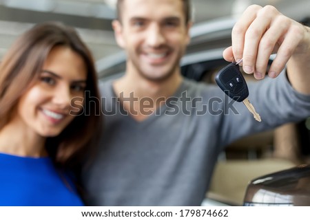 Key from a new car. Young couple standing near then new car and holding a key