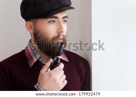 Smoking a pipe. Portrait of handsome young man in hat smoking a pipe and looking away