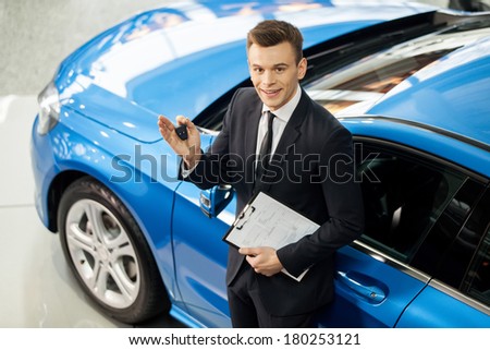 Let me assist you in your vehicle search. Top view of handsome young classic car salesman standing at the dealership holding a key