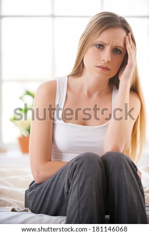 Feeling so badly. Frustrated young woman holding head in hand and expressing negativity while sitting in bed at her apartment
