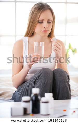 Taking medicines. Young woman drinking medicines while sitting in bed at her apartment
