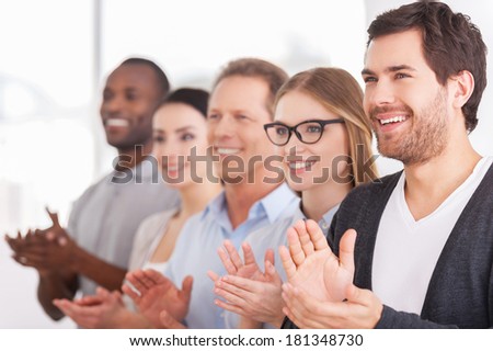 Applauding to corporate innovations. Group of cheerful business people applauding to someone  while standing in a row
