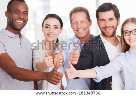 Happy business team. Group of cheerful business people in casual wear standing close to each other and showing their thumbs up