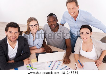 Strong business team. Top view of group of business people in casual wear sitting together at the table and smiling at camera