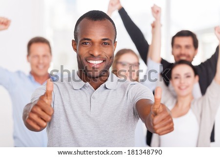 Happy business team. Happy young African man showing his thumbs up you and smiling while group of people in casual wear standing on background