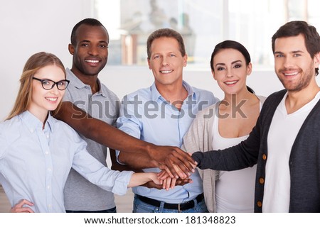Together we are stronger! Group of cheerful business people in casual wear standing close to each other and holding hands together