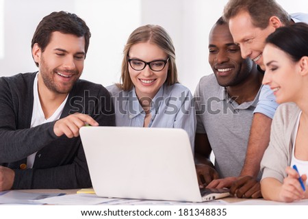 Creative team at work. Group of business people in casual wear sitting together at the table and discussing something while looking at the laptop