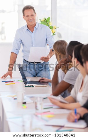 I have some good news! Group of business people sitting in a row at the table while mature man holding paper and smiling
