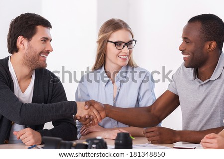 Friendly handshake. Two business people in casual wear handshaking while woman sitting between them and smiling