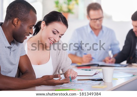 Creative team at work. Two business people sitting together at the table and discussing something while other people working on background