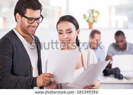 Working moments. Two cheerful business people holding documents and smiling while two people working on background