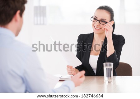 Interviewing a job candidate. Cheerful young woman in formalwear holding document and smiling while man sitting in front of her and gesturing