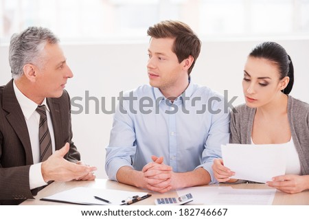 Financial consultation. Young couple sitting together at the table while senior man in formalwear telling something and gesturing