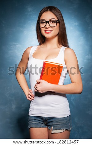 Confident and smart student. Cheerful young female student holding book and smiling