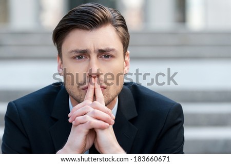 Thinking about solutions. Portrait of  young man in formalwear holding hands clasped and looking away while sitting outdoors