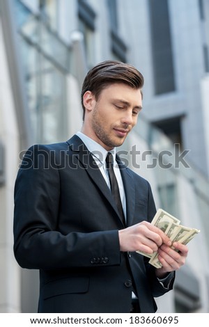 Young and wealthy. Confident young man in shirt and tie counting money and while standing outdoors