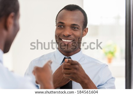 Feeling confident. Young African man adjusting his necktie and pointing himself at the mirror