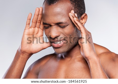 Awful headache. Portrait of shirtless African man touching head with hands and keeping eyes closed while standing against grey background