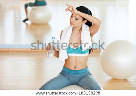 Tired after aerobics class. Top view of beautiful young woman in sports clothing drinking water and looking away