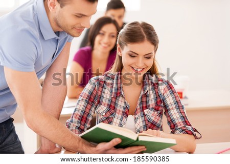 Students studying together. Two cheerful students discussing something while looking at the book together with other students sitting behind them