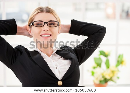 Chill time. Happy mature woman in formalwear holding hands behind head and smiling while sitting at her working place