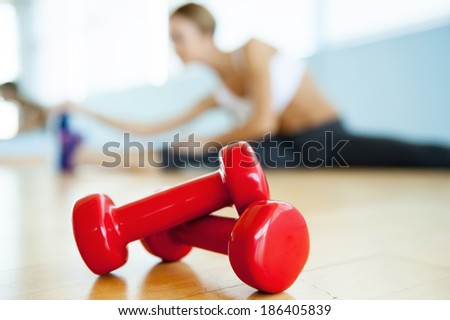 Sport and fitness concept. Close up image of dumbbell lying on the floor while young woman stretching on background