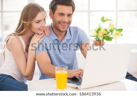 Surfing the net together. Cheerful young couple surfing the net together while sitting close to each other and looking at the laptop