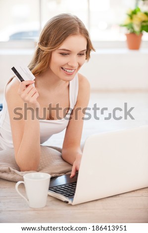 Shopping in the net. Beautiful young woman shopping in the net while holding a credit card and looking at the laptop