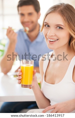 Starting morning together. Handsome young woman holding a glass of orange juice and looking over shoulder while having breakfast with his girlfriend