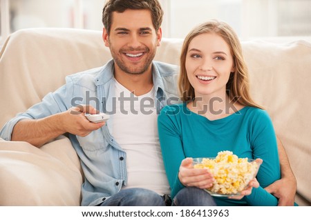 Watching TV together. Beautiful young couple sitting on the couch together and watching TV