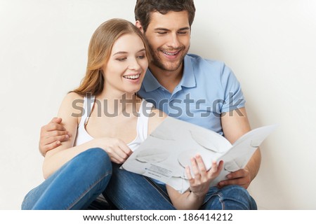 Beautiful loving couple. Beautiful young loving couple sitting on the floor and reading brochure together