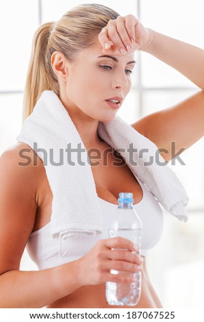 Relaxing after workout. Tired mature woman in sports clothing touching forehead with hand while holding a bottle with water