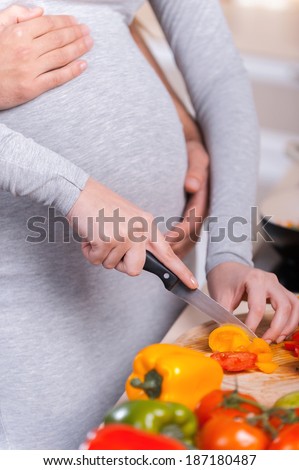 Only healthy food. Happy young couple cooking together in the kitchen while man touching abdomen of his pregnant wife