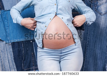 Pregnancy denim. Cropped image of woman in jeans clothes showing her pregnant belly while standing against jeans background