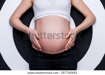 Pregnant belly. Cropped image of pregnant woman holding hands on belly while standing against target background