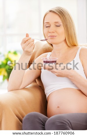 Pregnant woman day dreaming. Happy pregnant woman sitting on the chair and eating yogurt