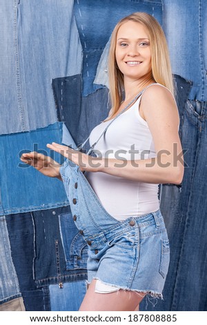 Always looking trendy. Side view of beautiful pregnant woman in jeans clothes posing while standing against jeans background