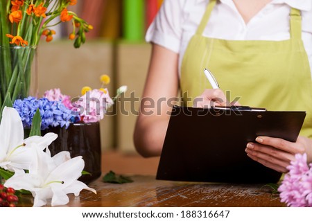 Female florist at work. Cropped image of female florist writing something at note pad while standing at her working place