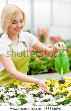 Flowers need my care. Beautiful blond hair woman in uniform watering flowers