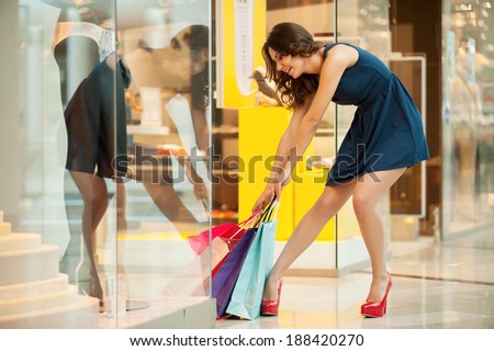 After day shopping. Full length of tired young woman in blue dress trying to pick up the heavy shopping bags