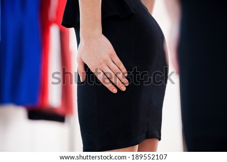 This dress fits me well! Cropped image of woman in black dress holding hands on hip while standing against the mirror