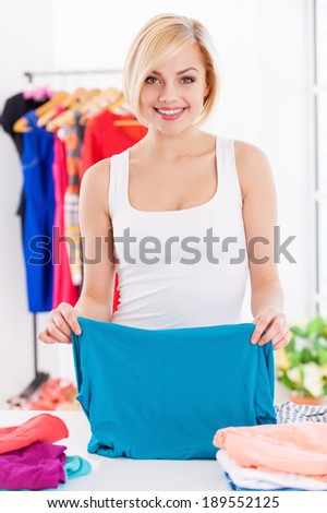 Woman folding clothes. Beautiful blond hair woman folding clothes and smiling at camera