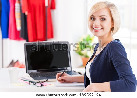 Confident and creative. Beautiful young woman looking over shoulder and smiling while sitting at her working place