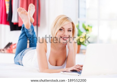Surfing the net at home. Beautiful young blond hair woman working at laptop while lying on the bed at home