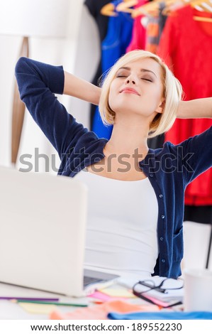 Relaxing at working place. Attractive young woman holding hands behind head and keeping eyes closed while sitting at her working place